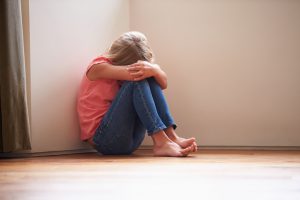Unhappy Child Sitting On Floor In Corner Crying To Herself At Home