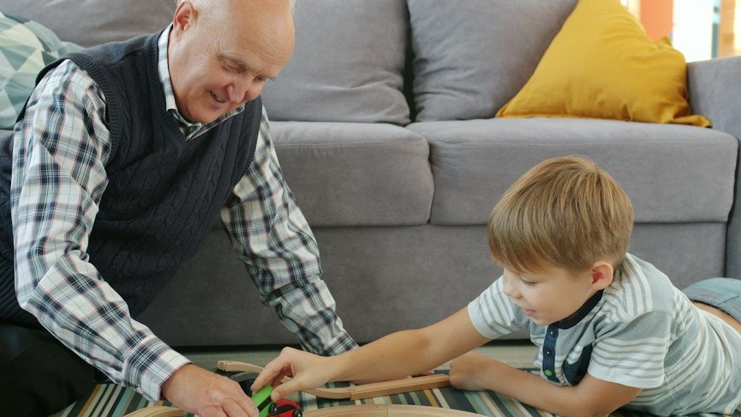 Bestefar og barnebarn leker sammen på gulvet foran sofaen
