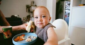 Småbarn smiler i barnestol med banan og mat på tallerkenen